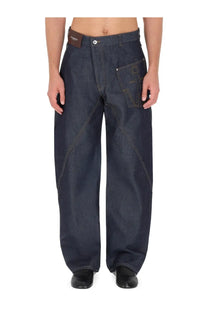 Jw Anderson men’s blue denim twisted workwear jeans with distinctive front pocket stitching and brown leather waistband tag