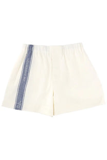 Cream-colored, elastic-waisted shorts with a navy blue vertical stripe featuring the ’jw anderson’ logo in white lettering.