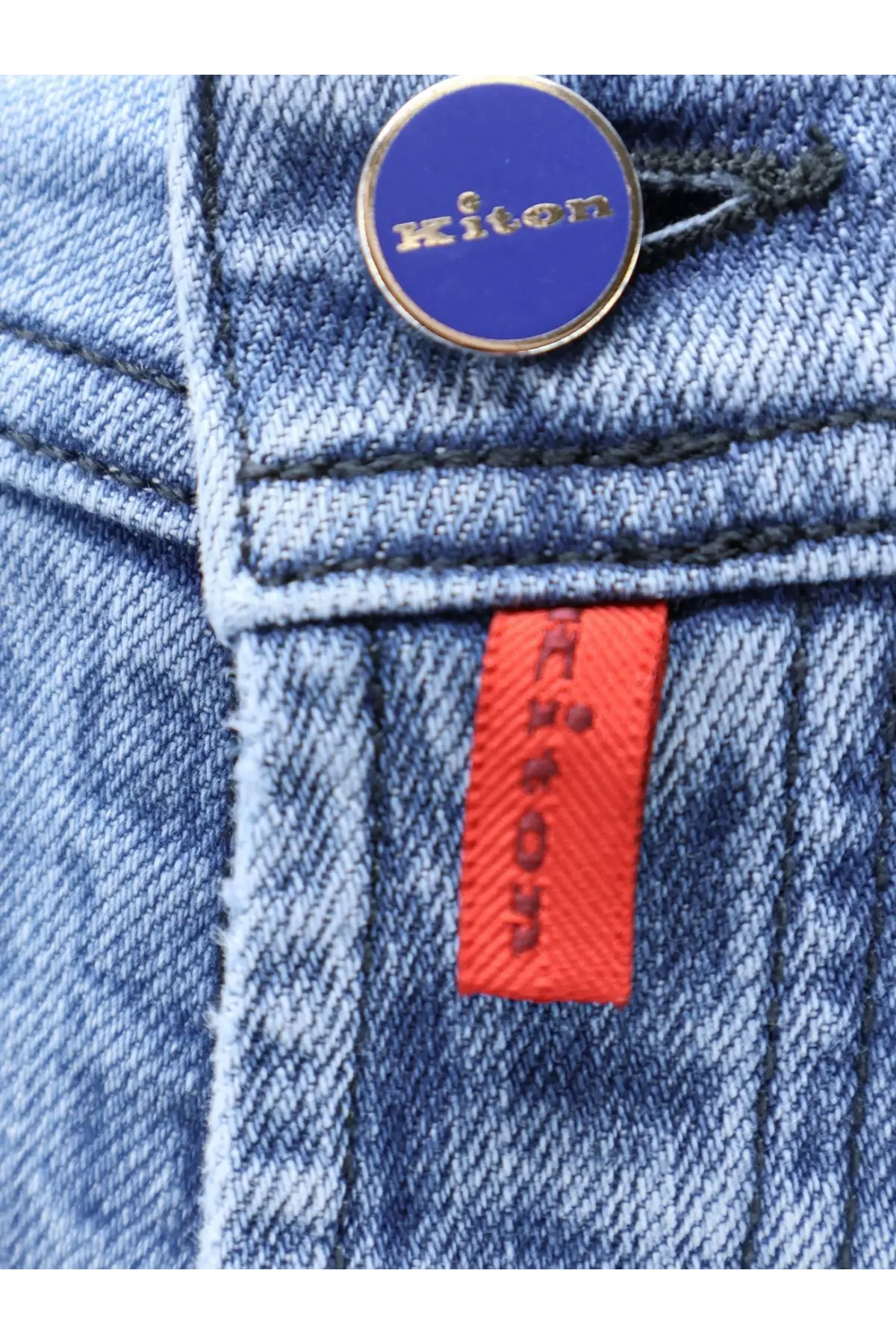 Kiton men’s blue denim jeans with circular blue and gold Kiton button and orange brand tag visible