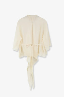 Cream-colored lightweight chiffon blouse with gathered neckline and asymmetrical ruffled hem tied at waist by lamrons