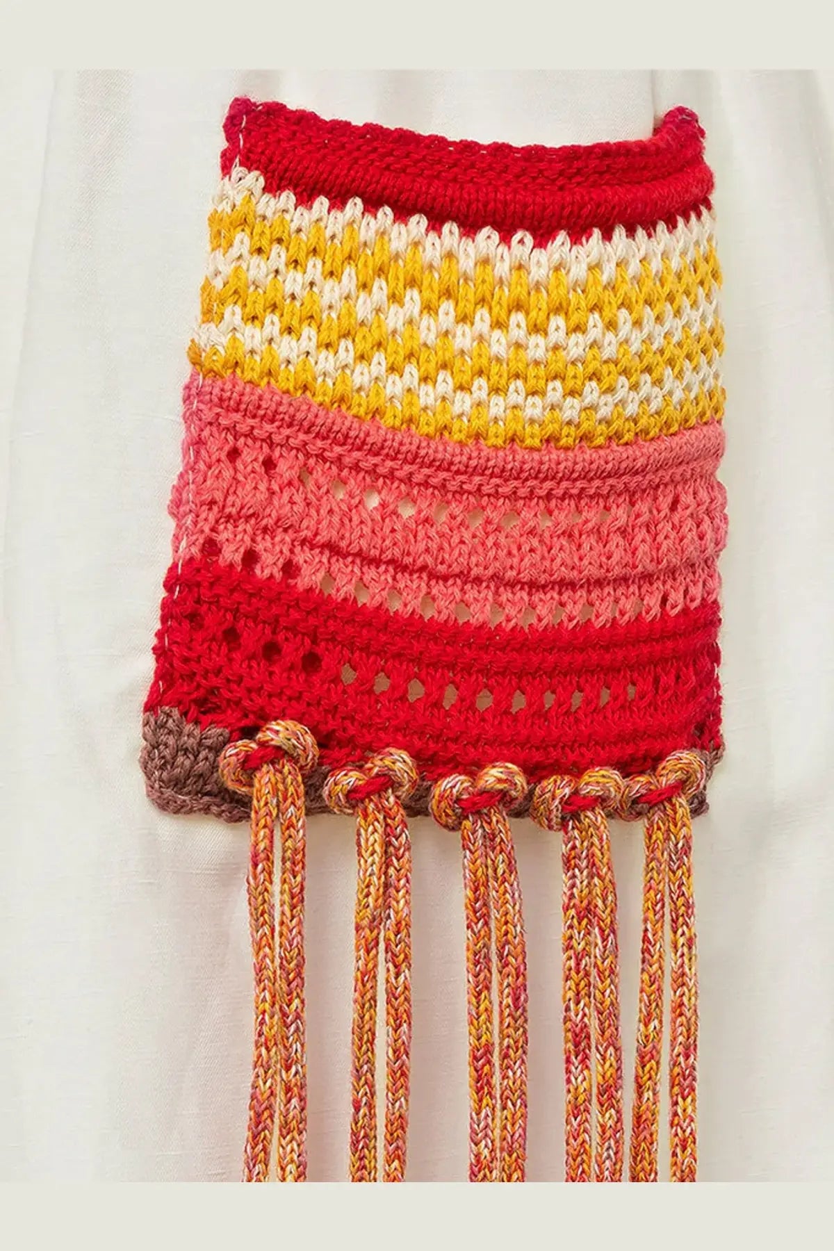 A hand-knitted multicolored fringe pouch with vibrant reds yellows and pinks paired with laneus women’s white viscose and linen blend cancun bermuda shorts