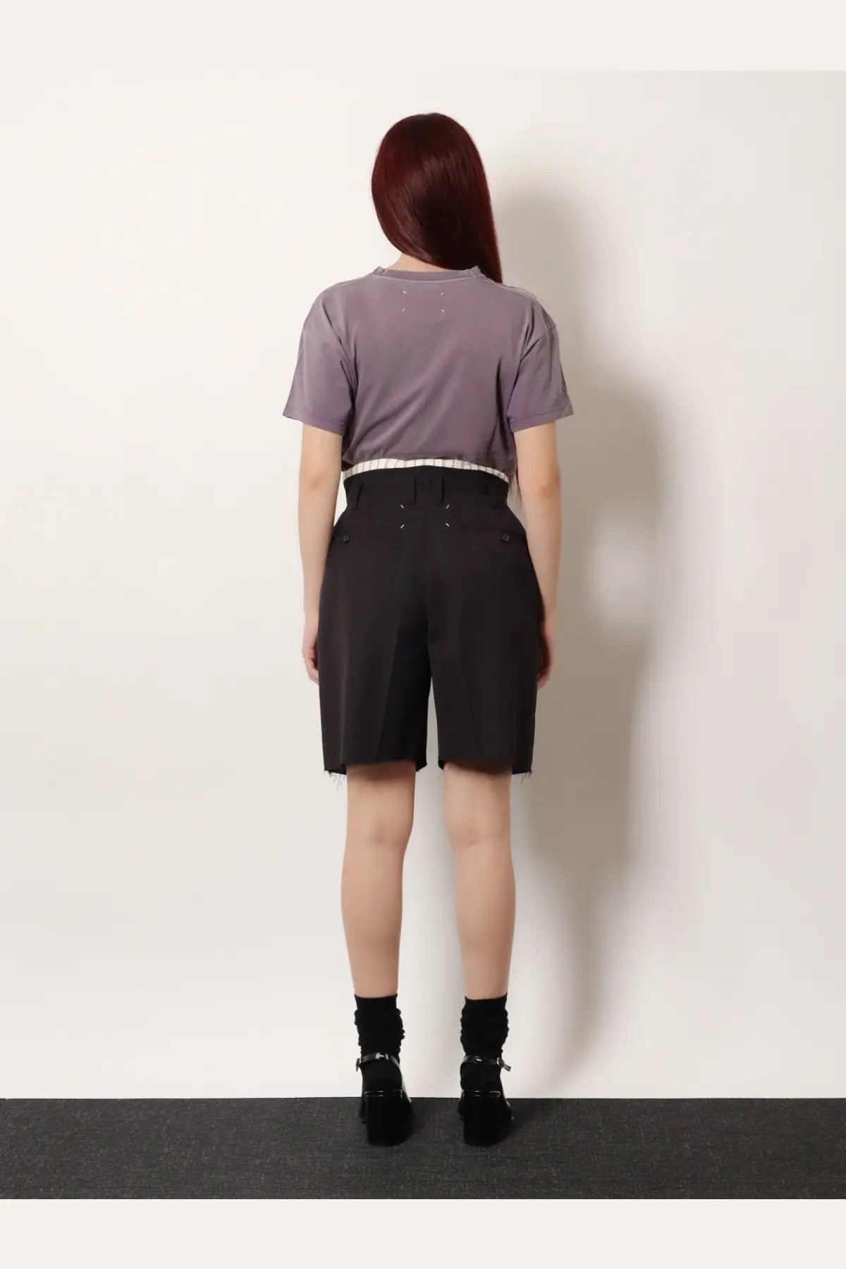 A person wearing maison margiela women’s black Virgin wool shorts with frayed hems and a lavender short-sleeved top