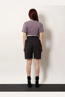 A person wearing maison margiela women’s black Virgin wool shorts with frayed hems and a lavender short-sleeved top