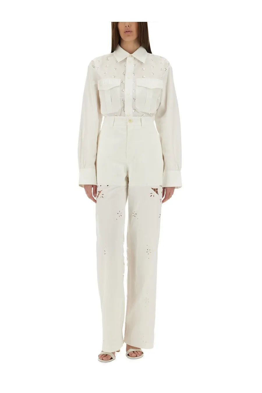 A cream-colored long-sleeved button-up shirt with floral embroidery and two front pockets paired with white upcycled linen pants by Marine Serre