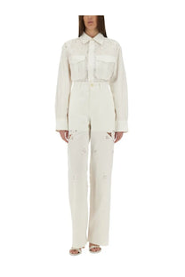 A cream-colored long-sleeved button-up shirt with floral embroidery and two front pockets paired with white upcycled linen pants by Marine Serre