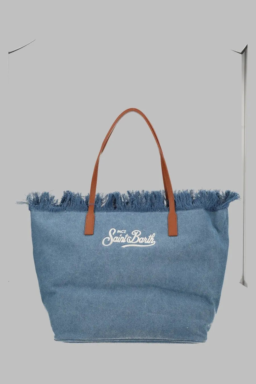 A light blue denim tote bag with brown leather handles and frayed top edge by mc2 saint barth