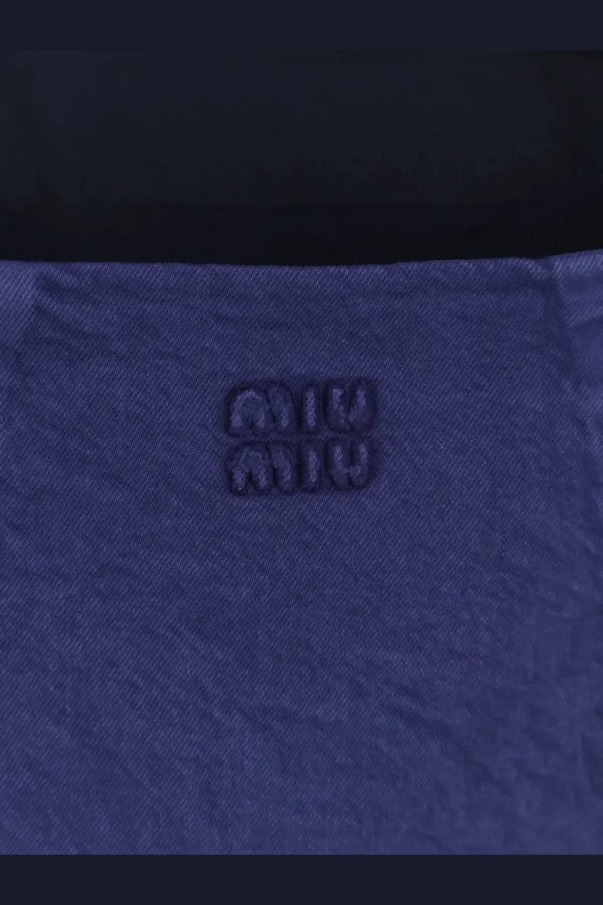 Deep blue denim fabric with subtle texture and embossed miu miu logo on miu miu women’s short denim dress inchiostro