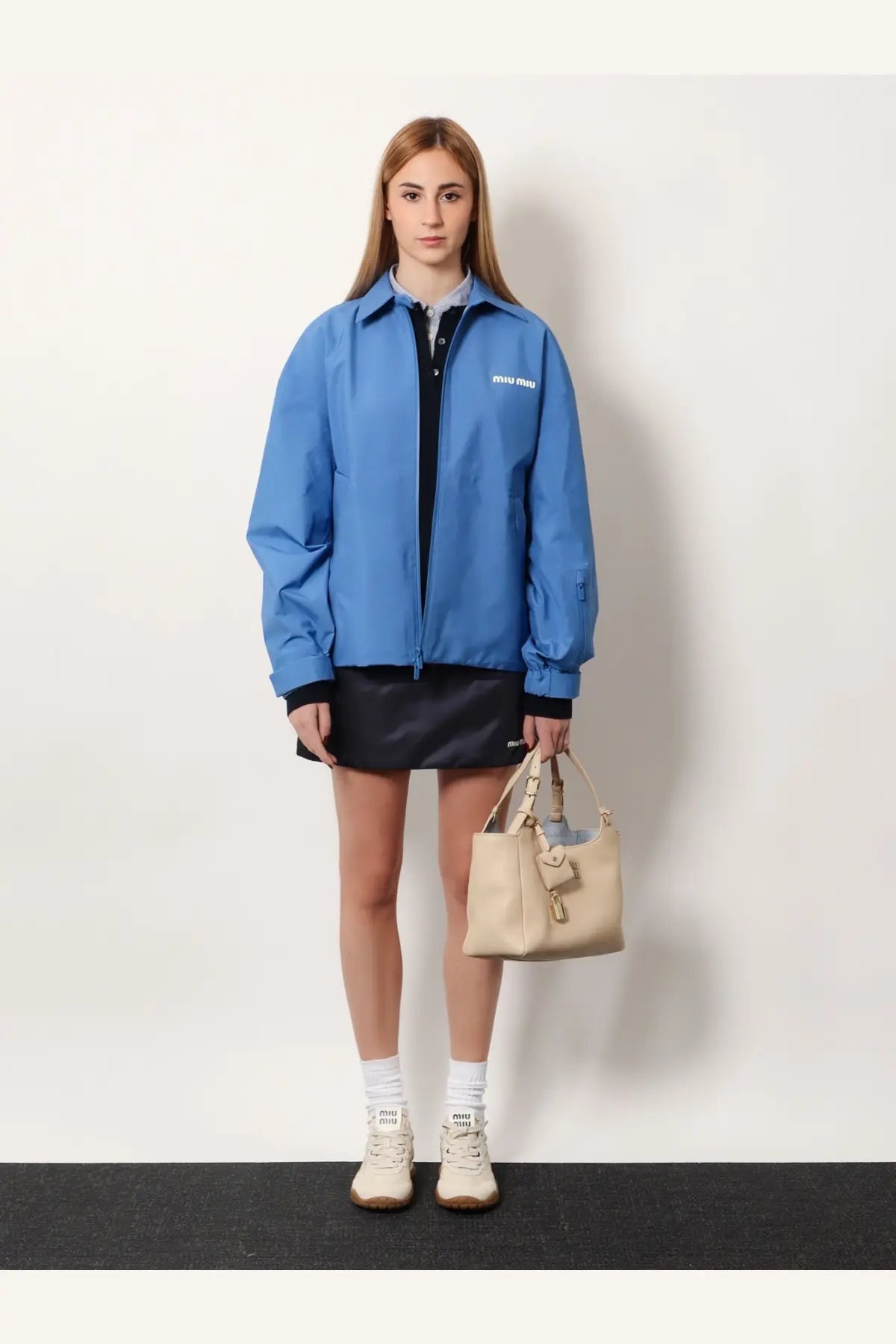 Beige leather miu miu tote bag with top handle and front flap closure paired with a purple technical fabric jacket