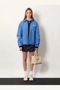 Beige leather miu miu tote bag with top handle and front flap closure paired with a purple technical fabric jacket
