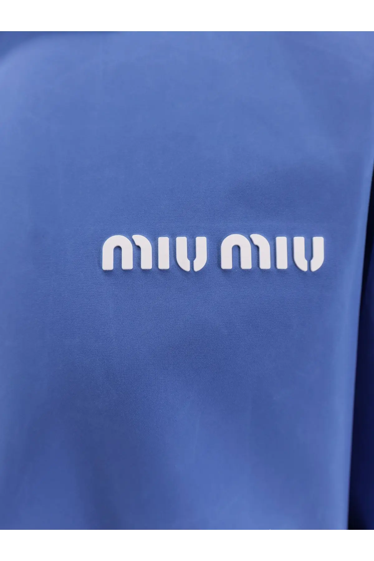 Blue miu miu logo patch with white raised lettering on textured fabric of a purple women’s technical fabric jacket