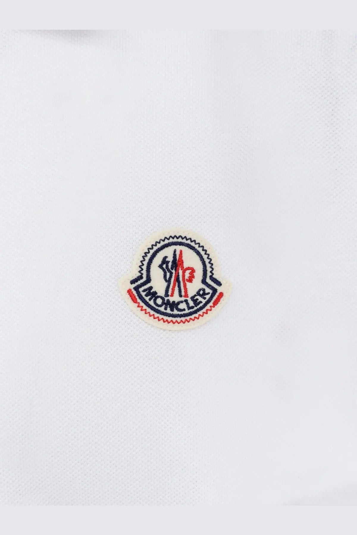 White moncler logo patch with red and navy blue embroidery on white fabric of men’s cotton polo shirt