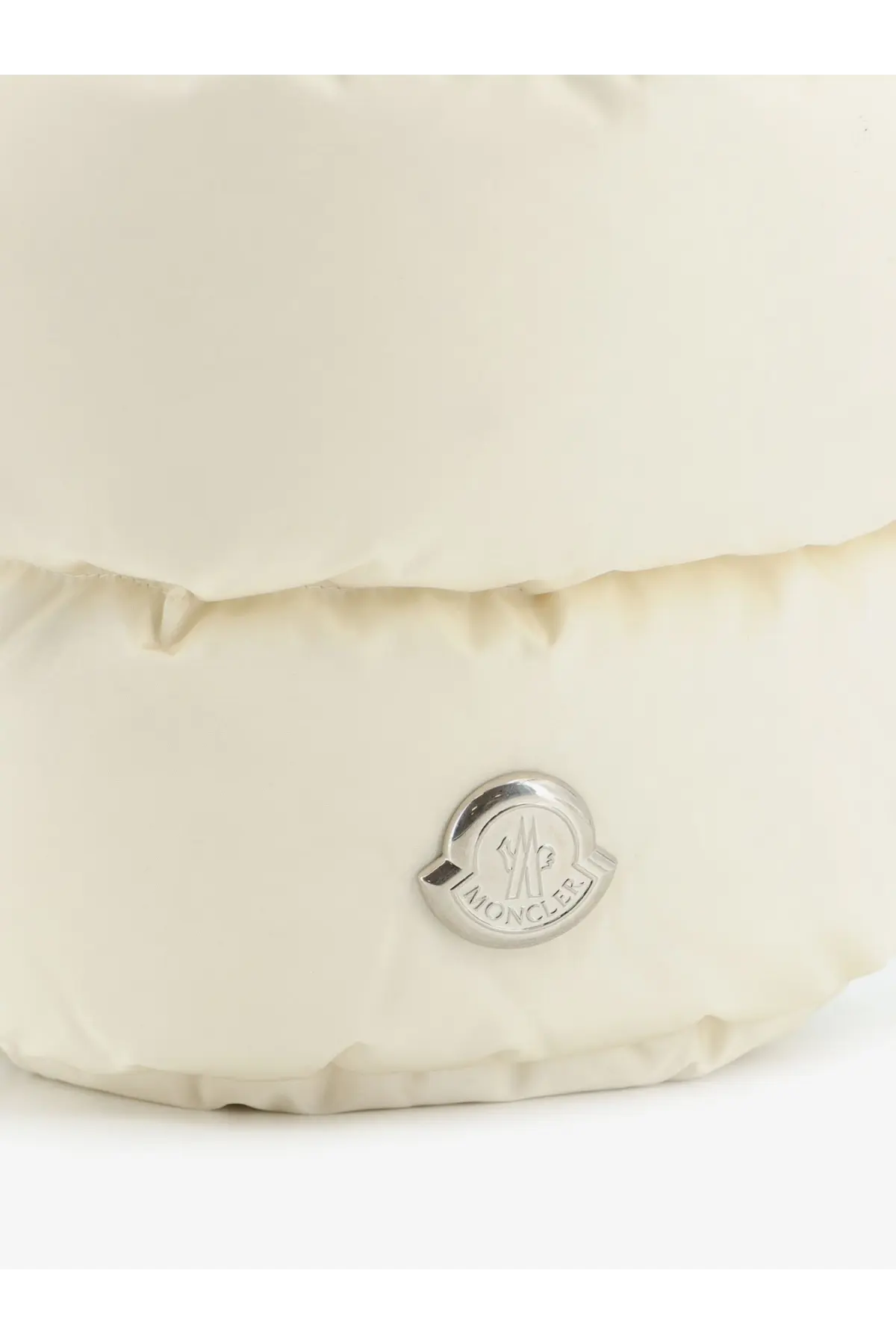 Cream-colored moncler puffer jacket with silver logo emblem in front featured with moncler women’s caradoc bucket bag