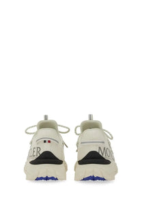 White moncler women’s trailgrip lite sneaker in beige with black and blue accents and textured rubber sole visible from back