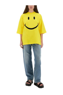Bright yellow oversized t-shirt with bold black smiley face graphic paired with moschino womens wide leg blue jeans