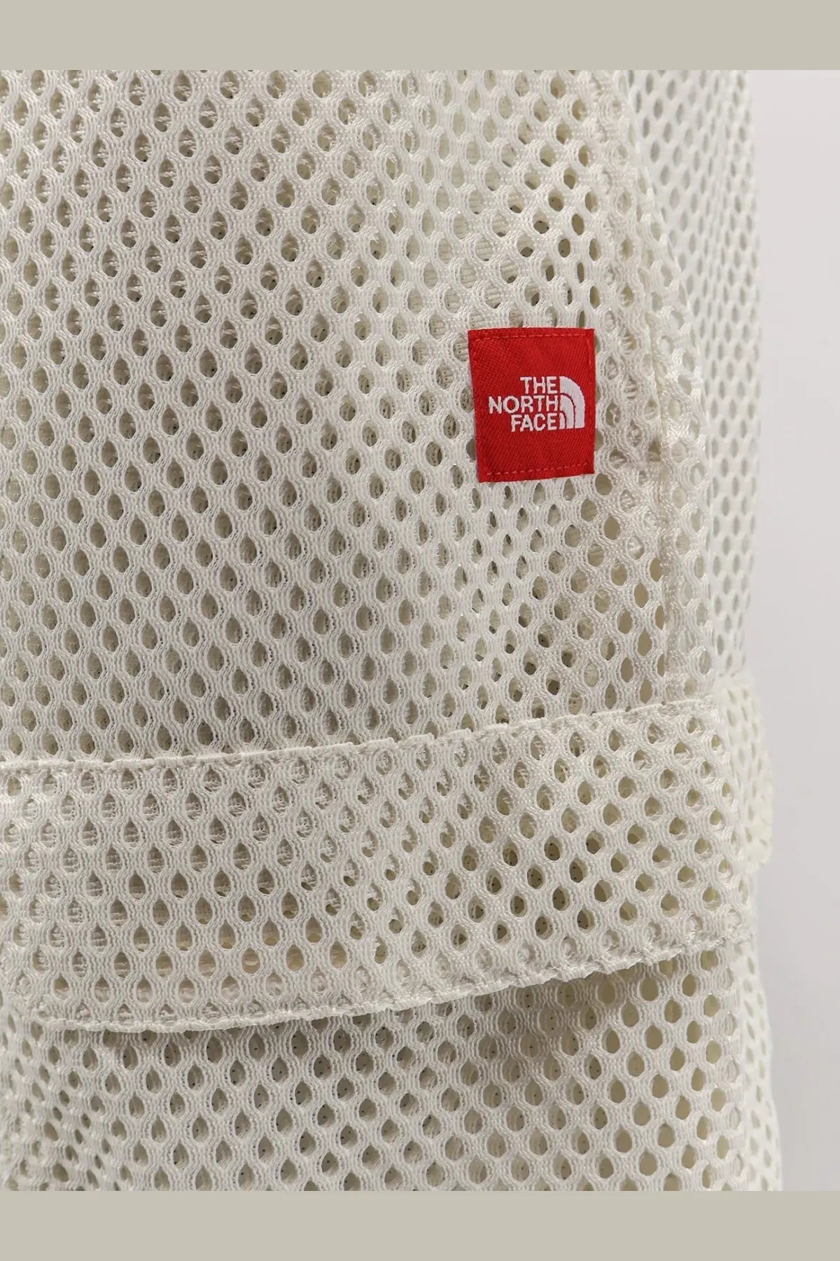 Off-white mesh fabric hat with red the north face logo patch paired with men’s white nylon bermuda shorts