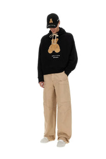 Palm Angels men’s black hoodie with plush tan bear appliqué and embroidered text paired with matching cap and cargo pants