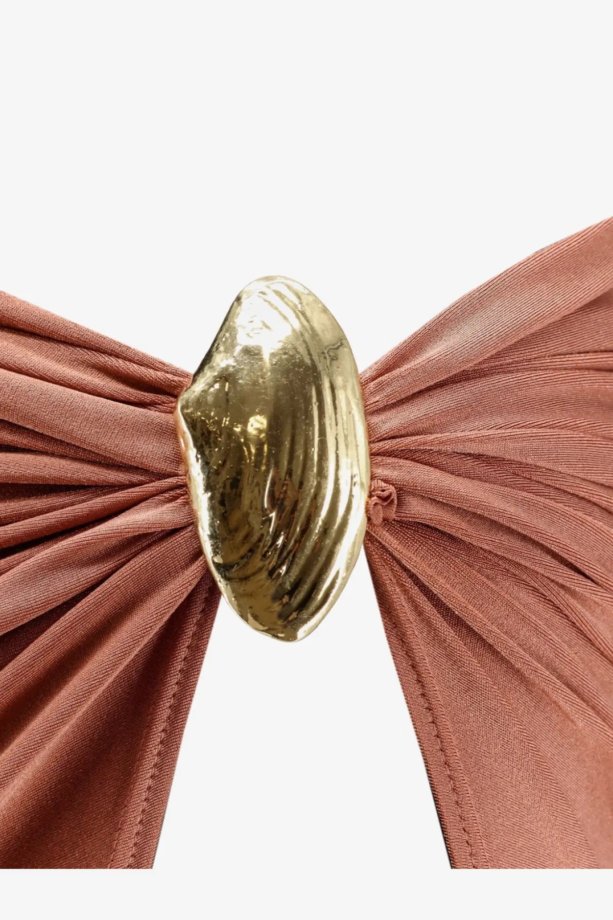A golden shell-shaped clasp fastening a rust-colored lycra skirt with gathered pleats from patbo women’s collection