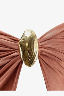 A golden shell-shaped clasp fastening a rust-colored lycra skirt with gathered pleats from patbo women’s collection