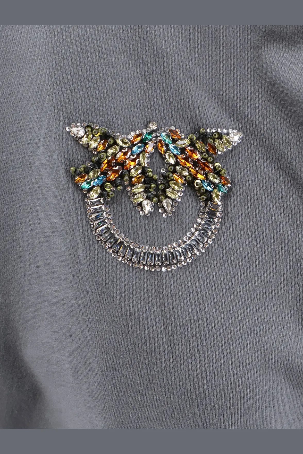 A sparkling multicolored rhinestone brooch shaped like a smiling face with wings on a pinko womens grey cotton shirt