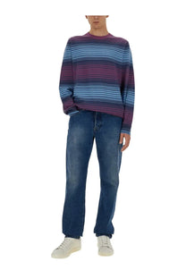A man wearing a ps by paul smith men’s multicolor striped long-sleeved sweater with purple and light blue bands paired with dark wash jeans