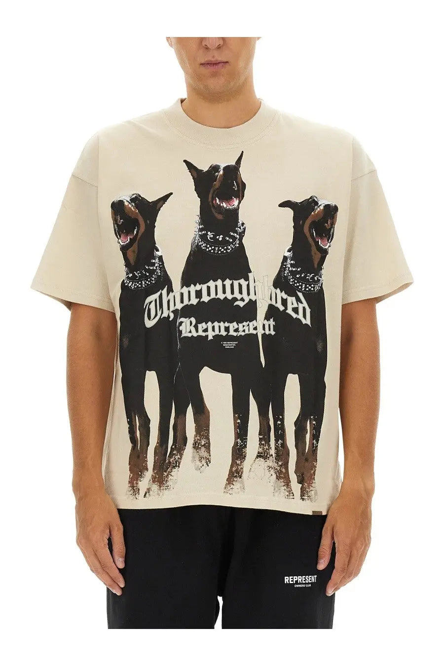 Cream-colored oversized men’s t-shirt featuring bold graphic of three black doberman pinschers with studded collars and thoroughbred represent text