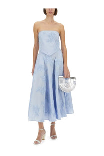 A silver fan-shaped clutch with a sleek modern design and distinctive u-form handle paired with a blue floral maxi skirt