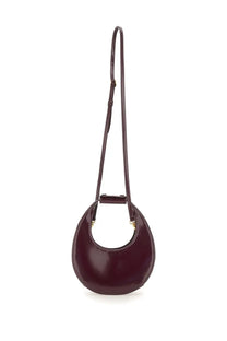 Staud women’s mini moon bag in glossy burgundy leather with minimalist circular design and adjustable slender strap