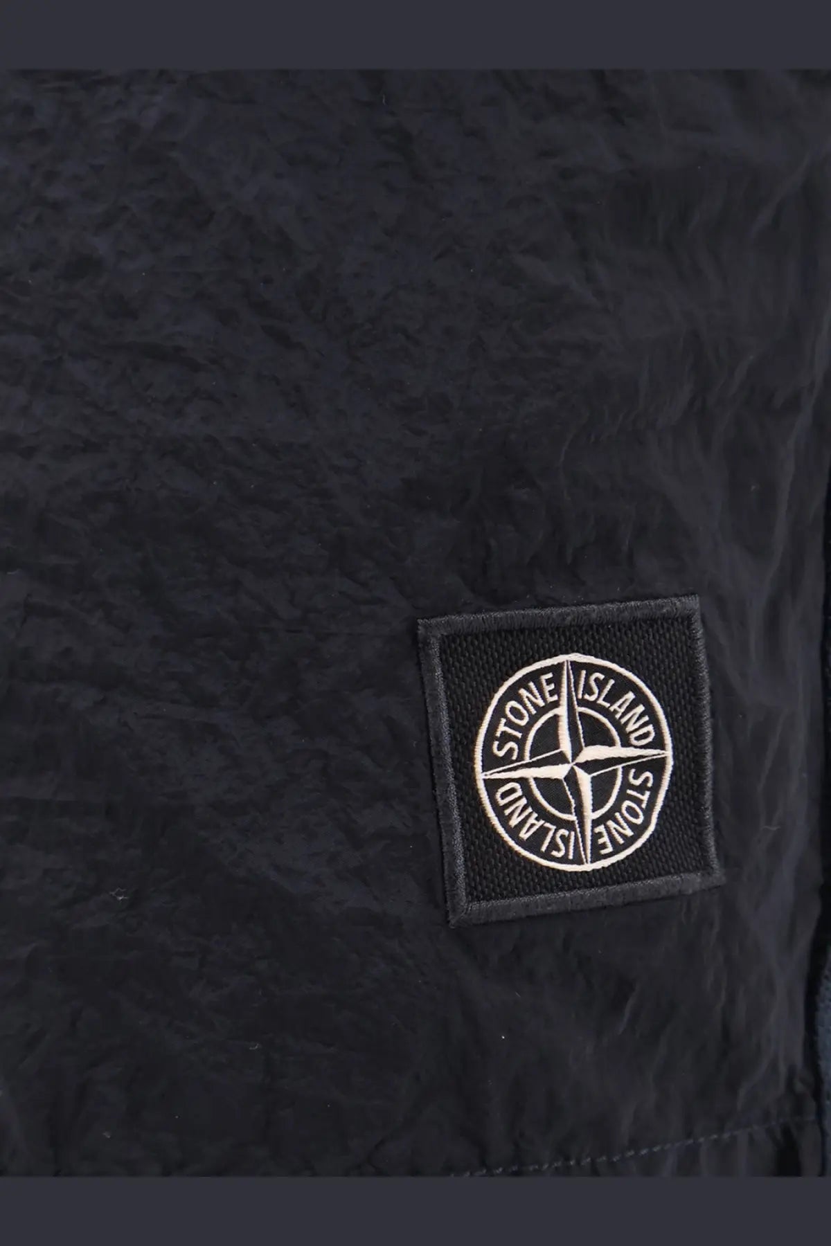Black stone island patch with white embroidered logo on textured fabric on stone island men’s econylon swim trunks blue