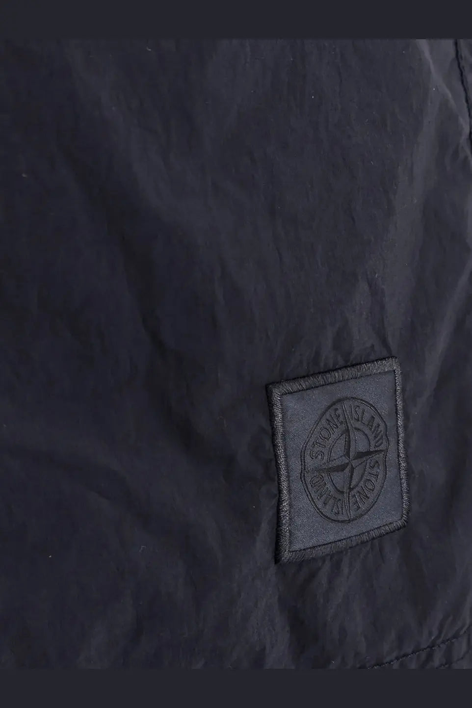 Black stone island embroidered logo patch on dark fabric of stone island men’s blue nylon swim trunks