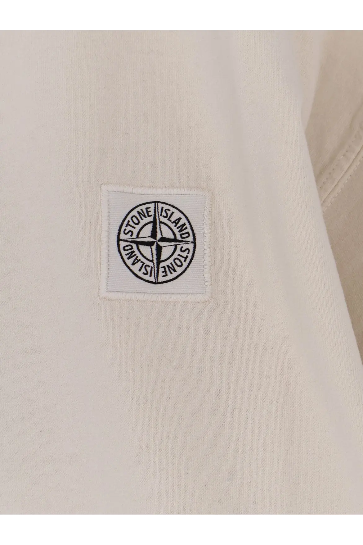 White stone island patch with black embroidered compass rose on light fabric of stone island men’s organic cotton shirt