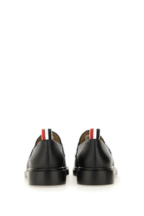 Back view of thom browne men’s black leather moccasin penny loafer with red white and blue striped tab at heel