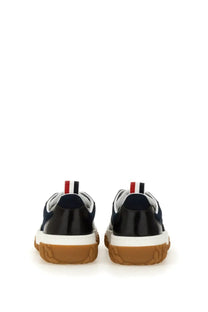 Navy blue and black Thom Browne men’s trainer with white midsole tan rubber outsole and red white blue heel pull tab