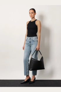 Black leather hobo bag with structured minimalist design and single top handle paired with toteme womens grey organic cotton jeans