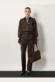 Brown suede shoulder bag with flap closure and adjustable strap shown with Toteme women’s grey tie cuff wool shirt