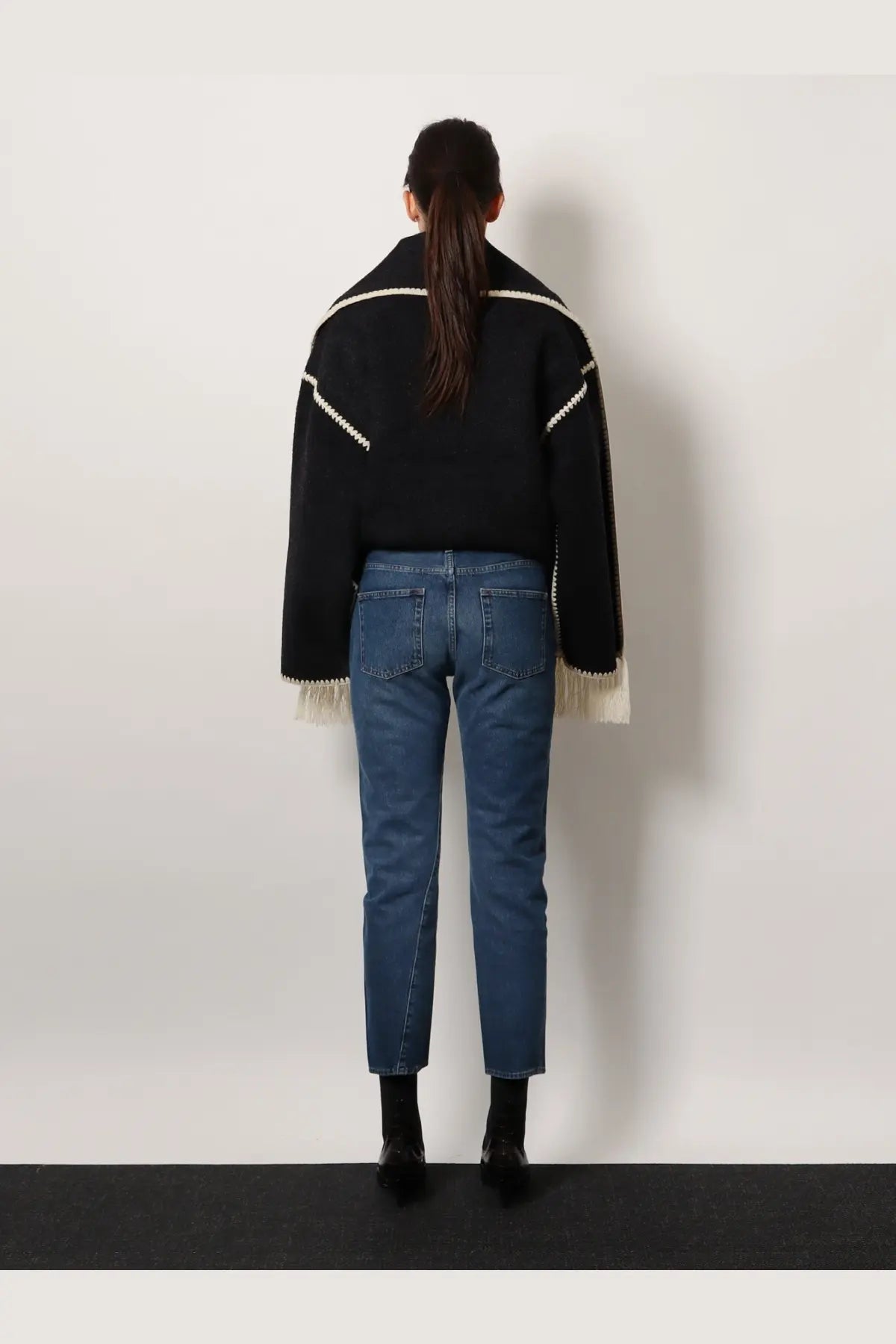 Black knit sweater with white geometric trim and fringed cuffs paired with toteme women’s twisted seam jeans blue