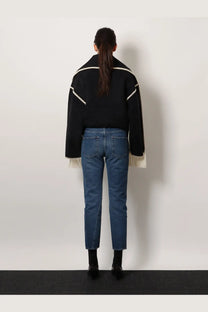 Black knit sweater with white geometric trim and fringed cuffs paired with toteme women’s twisted seam jeans blue