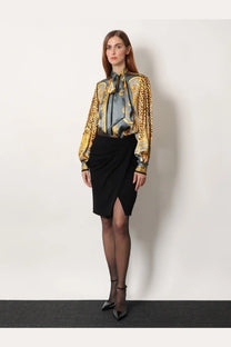 A woman wearing a luxurious satin blouse with gold and gray baroque pattern and leopard print cuffs with a versace black stretch viscose midi skirt