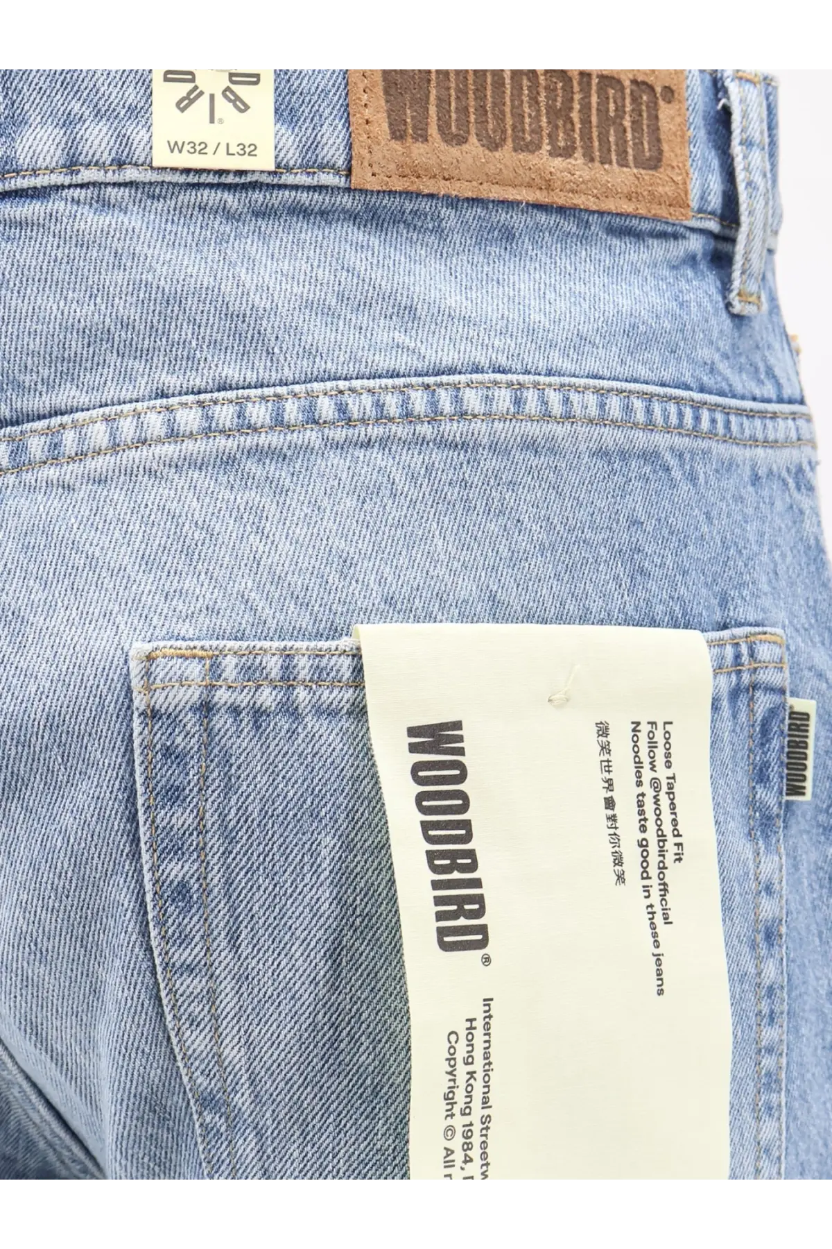 Light-wash denim jeans with brown leather woodbird patch and white paper tag showcasing the brand logo