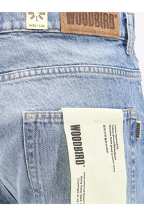 Light-wash denim jeans with brown leather woodbird patch and white paper tag showcasing the brand logo