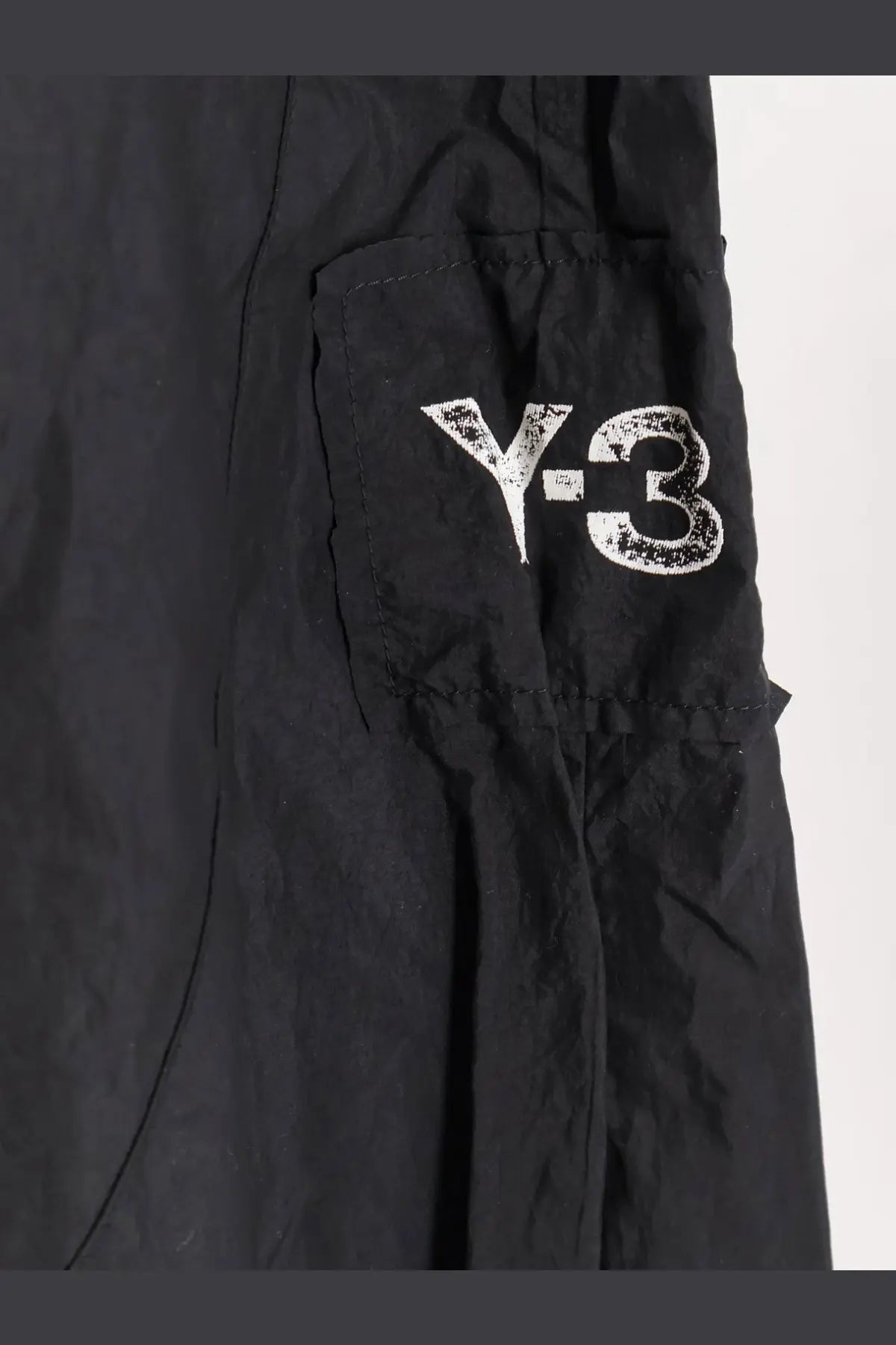 Black y-3 men’s baggy nylon cargo trousers with a distressed white logo on the side pocket
