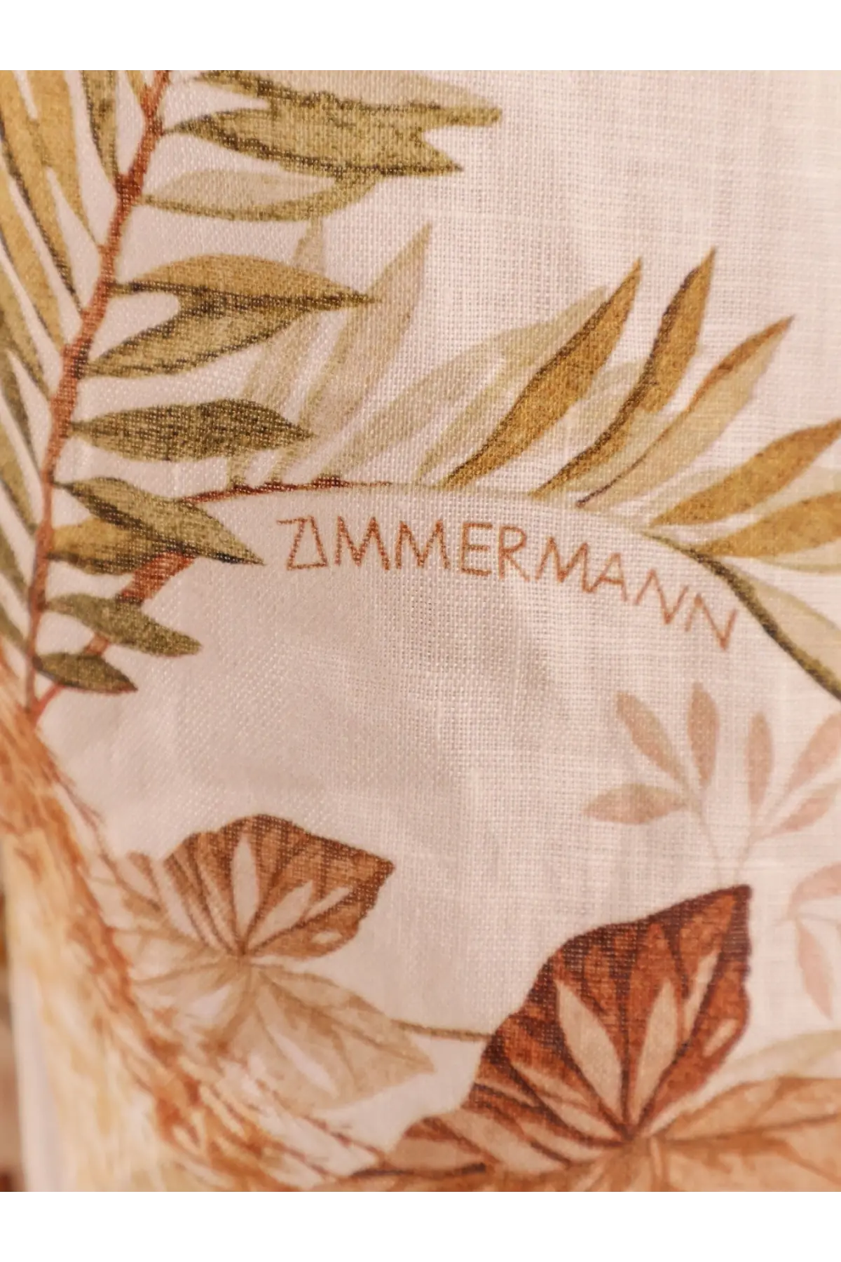 A beige zimmermann scarf with delicate olive gold and brown botanical print paired with a white linen midi dress